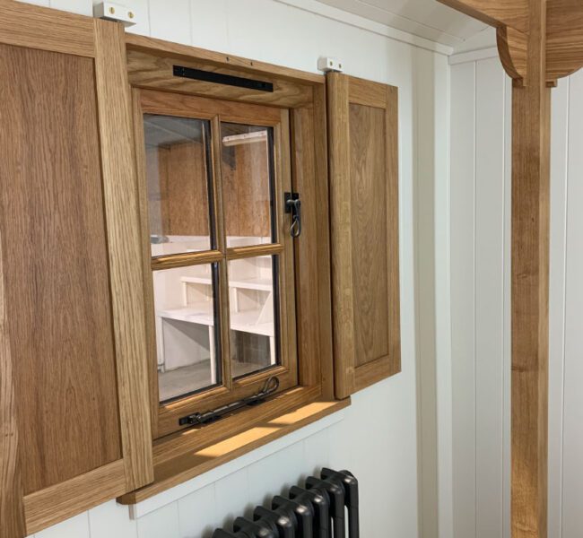 Wood-framed window with open shutters inside a white-panelled room, above a black cast iron radiator.